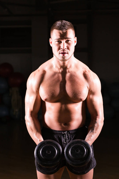 Sportos félmeztelen fiatal férfi fitness modell rendelkezik a súlyzók. - Fotó, kép