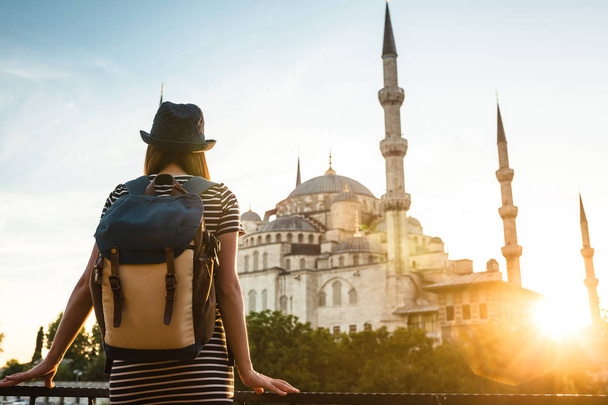 Молодая красивая девушка-путешественница в шляпе с рюкзаком, смотрящая на голубую мечеть - известную туристическую достопримечательность Стамбула. Путешествия, туризм, осмотр достопримечательностей
. - Фото, изображение