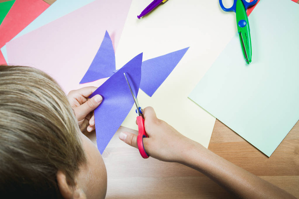 Αγόρι κοπής χρωματιστό χαρτί με το ψαλίδι στο τραπέζι - Φωτογραφία, εικόνα