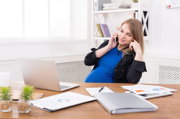 Беременная деловая леди на работе разговаривает по телефону
 - Фото, изображение