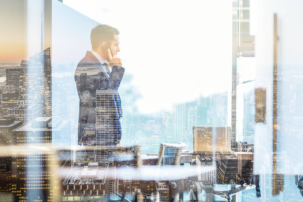 Hombre de negocios hablando en un teléfono móvil mientras mira a través de la ventana en NY - Foto, imagen