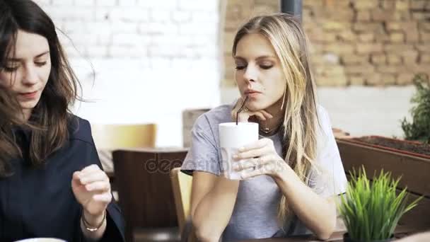 Two girlfriends in a cafe looking at a smartphone and drinking beverages - Footage, Video