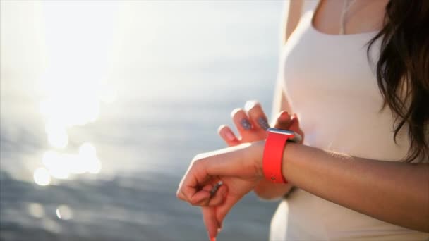Bliska strzał kobieta ręce przy użyciu Inteligentne zegarki naprzeciwko morza podczas zachodu słońca. - Materiał filmowy, wideo