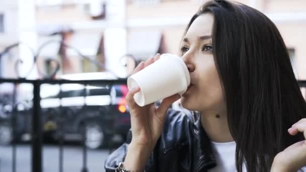 Black haired woman drinking a coffee to go in a cafe outdoors - 映像、動画