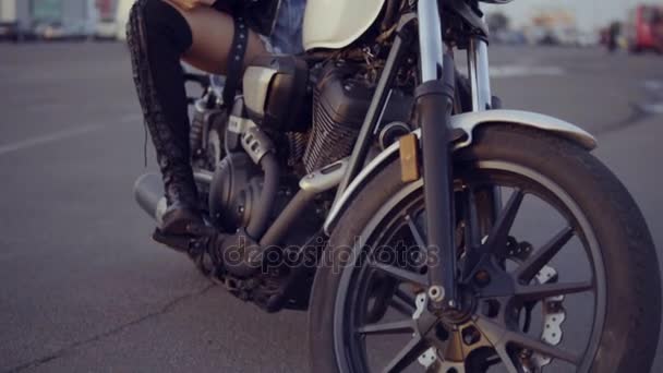 Pretty female biker in shorts sitting on the motorcycle seat and holding her helmet. Youn curly woman in sunglasses looking in the camera - Video, Çekim