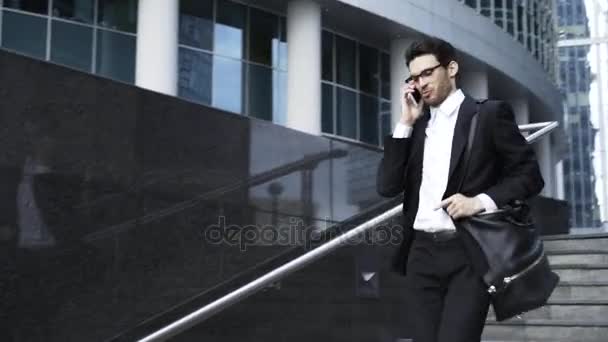 Jonge knappe zakenman in glazen naar beneden gaan en spreken op de telefoon - Video