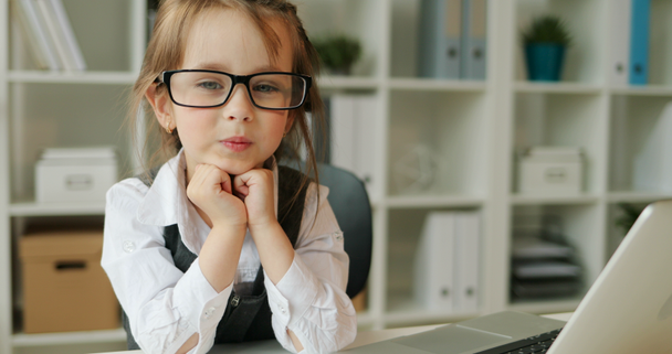 Caucasian girl siting on the desk in modern office. Young girl with glasses posing on the camera and smiling on office background. Close up. Indoor. - Πλάνα, βίντεο