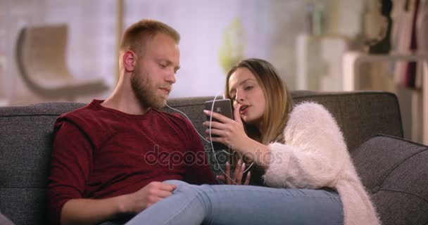 Modern couple with earphones looking at smartphone - Кадри, відео