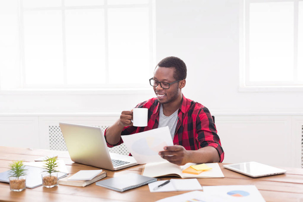 Homem de negócios preto no escritório casual, local de trabalho com laptop e papelada
 - Foto, Imagem