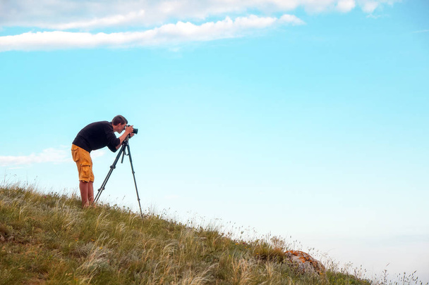 Un photographe avec un trépied et un appareil photo fait des photos de paysages sur la montagne
 - Photo, image