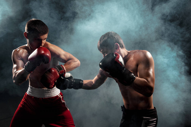 Two professional boxer boxing on black smoky background, - Foto, afbeelding
