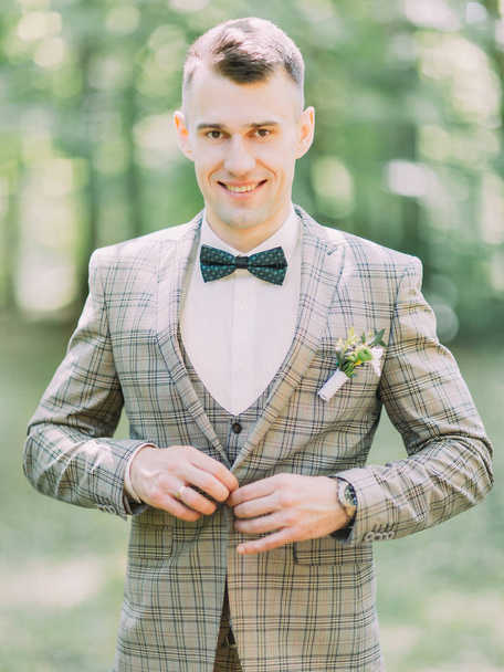 The smiling groom is buttoning his wedding jacket. - Fotó, kép