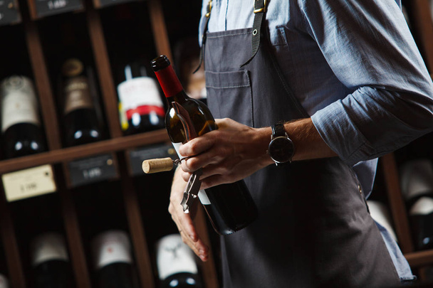 Sommelier holding wine bottle in cellar on background of shelves - Фото, изображение