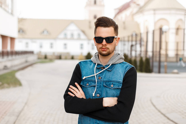 Handsome man in sunglasses and a jeans jacket posing on the street - Foto, Imagen