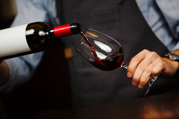 Man pouring wine into wineglass, male hand holding bottle - 写真・画像