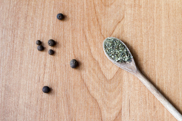 Composition of a wooden spoon with green spices and small black  - Photo, image