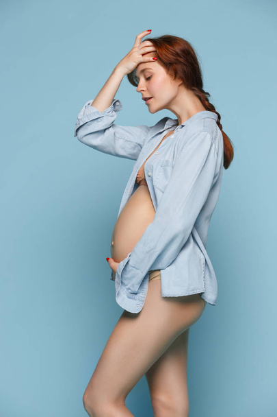 Young beautiful pregnant woman standing on blue background - 写真・画像