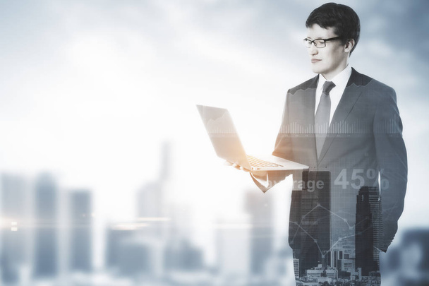 Handsome businessman using laptop on blurry city backgroud with copy space and business charts. Accounting concept. Double exposure - Photo, Image