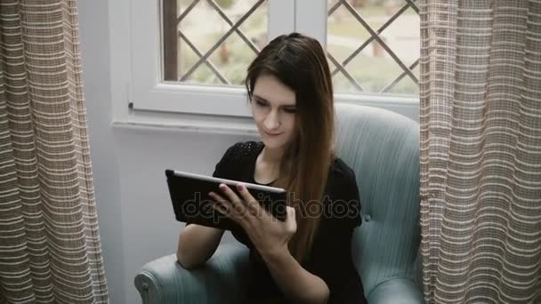 Mladá krásná brunetka surfování na internetu a pomocí tabletového počítače za to. Atraktivní dívka odpočívá doma. - Záběry, video