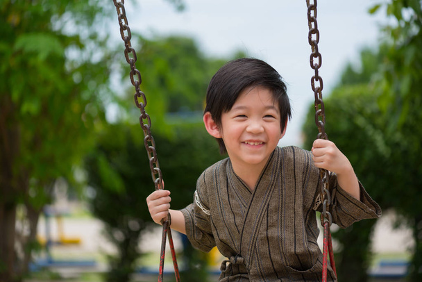 Lähikuva onnellinen aasialainen poika pukeutua japanilainen kangas pelaa swing puistossa
. - Valokuva, kuva