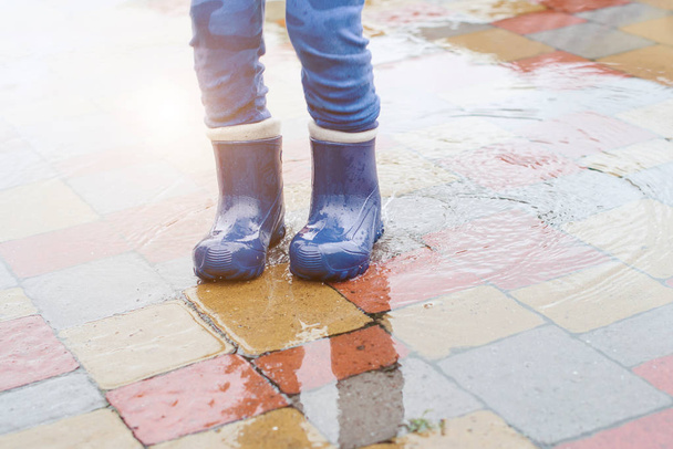 Voeten van kind in rubberen laarzen in een plas springen na regen. - Foto, afbeelding