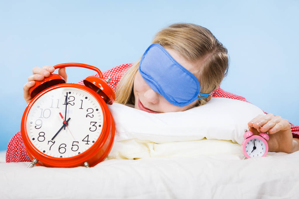 Спляча жінка в піжамі тримає годинник
 - Фото, зображення