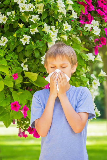 Alergii. Dziecko jest dmuchanie nosa w pobliżu kwitnących kwiatów - Zdjęcie, obraz