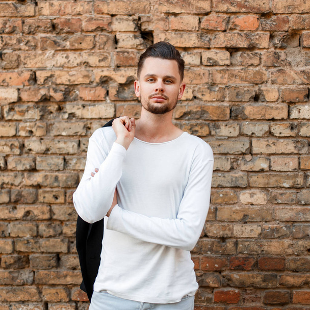 Handsome fashionable man with a haircut in a white shirt near a brick wall - Photo, Image