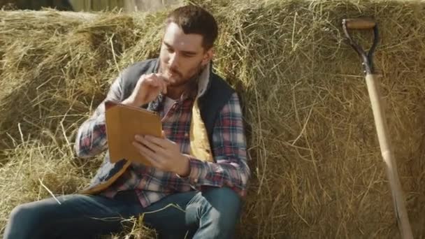 Farmer is sitting in hay and using a tablet computer. - Filmmaterial, Video