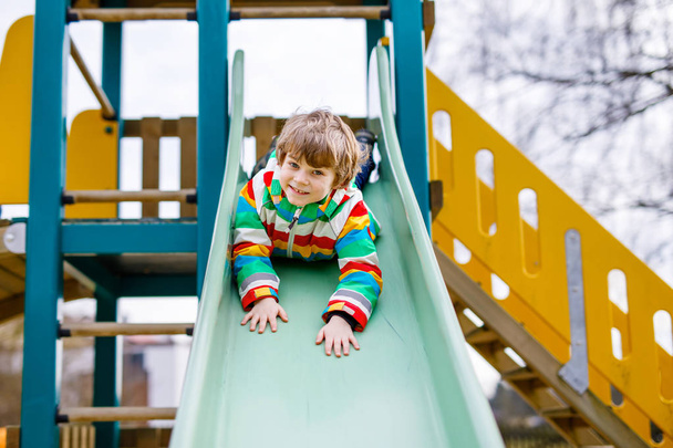 Happy blond kid boy having fun and sliding on outdoor playground - Photo, Image