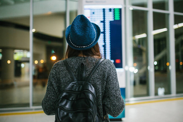 Chica joven viajero con una mochila en un sombrero mira el tablero de información en el aeropuerto. Obtener información sobre el vuelo. Transferencia
. - Foto, imagen