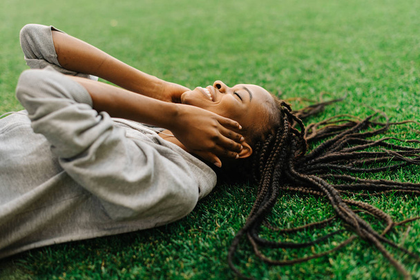 Gros plan sur le côté portrait de la charmante afro-américaine souriante jouissant de la musique dans les écouteurs tout en étant allongé sur l'herbe
. - Photo, image