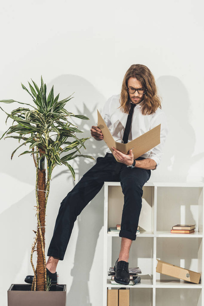 Businessman with folder sitting on bookshelf - Photo, Image