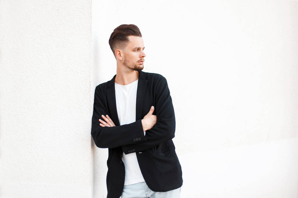 Hombre guapo y elegante con peinado en ropa de moda de negocios cerca de la pared blanca
 - Foto, imagen
