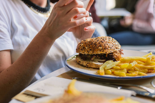 Mooie vrouw hamburger en chips eten in restaurant - Foto, afbeelding