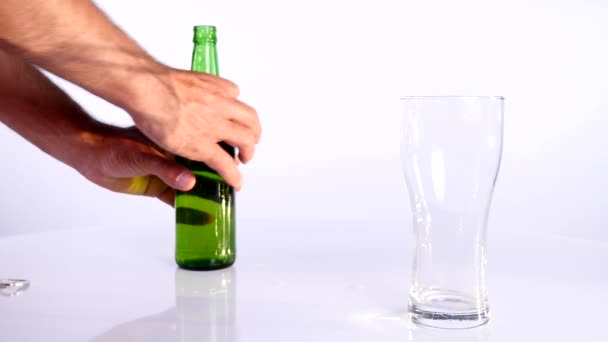 A bottle of beer is poured into a cup on a white background - Кадры, видео