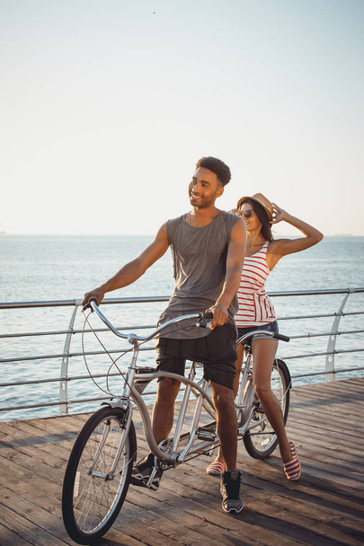 Portrait of a mixed race couple on tandem bicycle outdoors near the sea - Фото, зображення