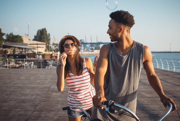 Portrait of a mixed race couple having fun on tandem bicycle outdoors near the sea - Foto, Imagen