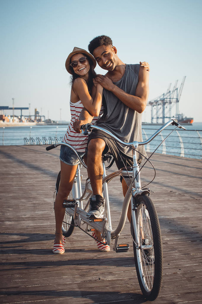 Portrait of a mixed race couple on tandem bicycle outdoors near the sea - Zdjęcie, obraz