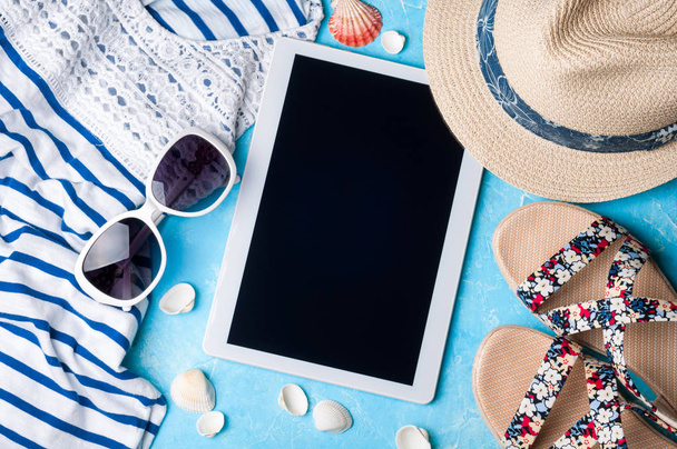 Accesorios para mujer de verano: gafas de sol, sombrero, sandalias, camisa y tablet sobre fondo azul. Concepto de vacaciones, viajes y trabajo freelance
 - Foto, Imagen