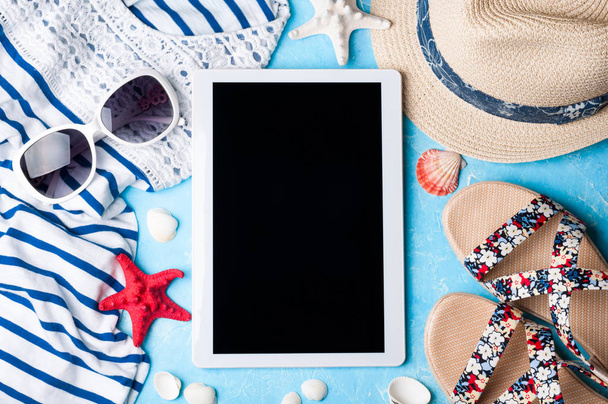 Acessórios femininos de verão: óculos de sol, chapéu, sandálias, camisa e tablet em fundo azul. Conceito de férias, viagens e trabalho freelance
 - Foto, Imagem