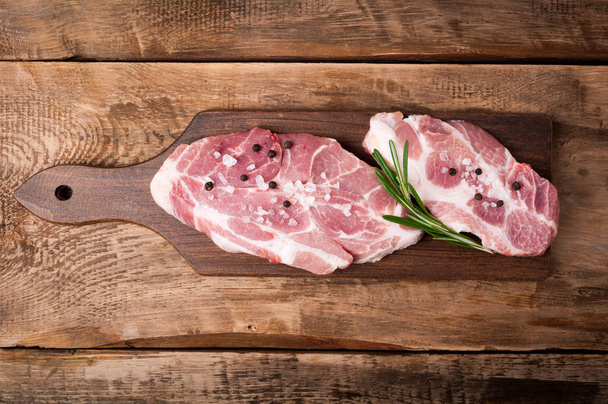 Carne crua. Bife de porco com ervas e especiarias na tábua de corte sobre fundo de madeira rústica
 - Foto, Imagem