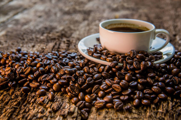 Café. Uma xícara quente de café e grãos de café torrados em uma mesa de madeira. Fundo escuro
 - Foto, Imagem
