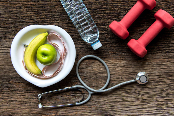 Ernährung und Gewichtsabnahme für eine gesunde Pflege mit medizinischem Stethoskop, Fitnessgeräten, Messhahn, Süßwasser und grünem Apfel auf hölzernem Hintergrund von oben. Gesundes Konzept. - Foto, Bild