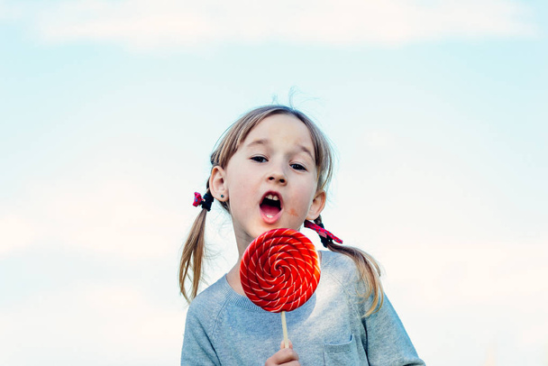 little caucasian girl with big candy making funny faces - Foto, imagen