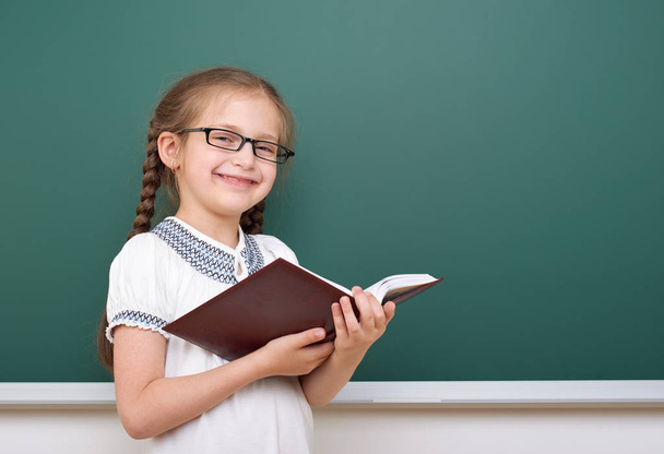 School girl read book, posing at school board, empty space, education concept - Фото, изображение