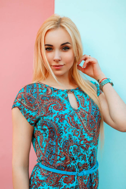 Gyönyörű fiatal nő, egy világos kék nyári ruha egy mintával, világos rózsaszín fal közelében - Fotó, kép