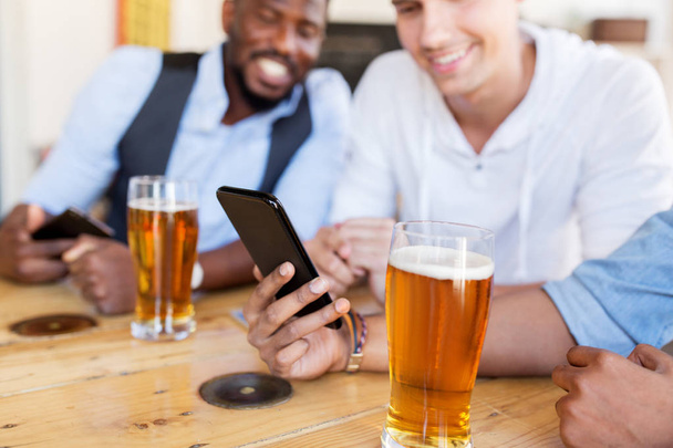 male friends with smartphone drinking beer at bar - Fotografie, Obrázek