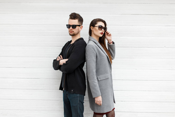 Beautiful fashionable couple models with sunglasses posing near white wooden wall - Photo, Image