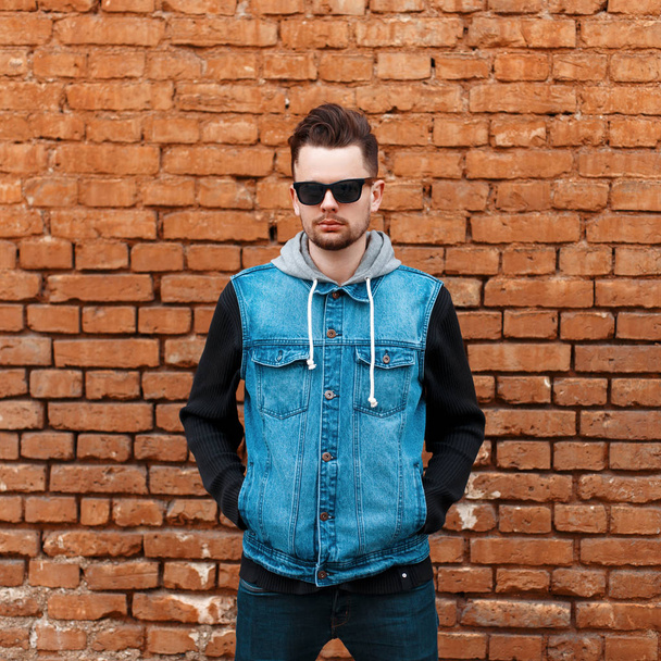 Guapo hipster chico en una chaqueta de mezclilla cerca de una pared de ladrillo
 - Foto, Imagen